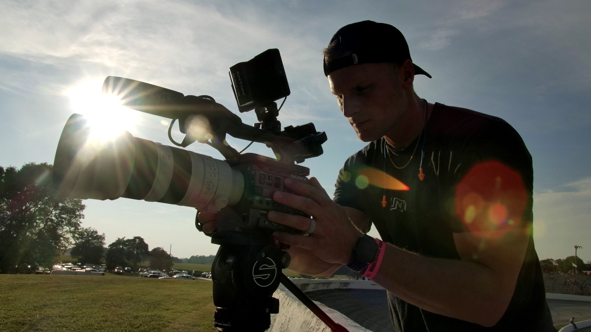 Josh Nagel operating a Sony cinema camera and monitor at a racetrack at golden hour, backlit by the sun.