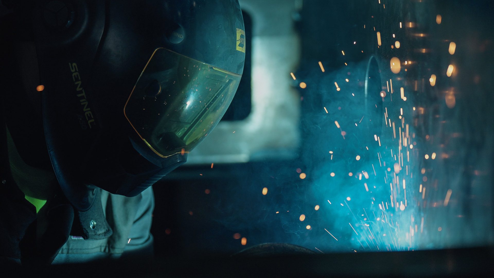 Welder at work, lit by blue light and bright sparks.